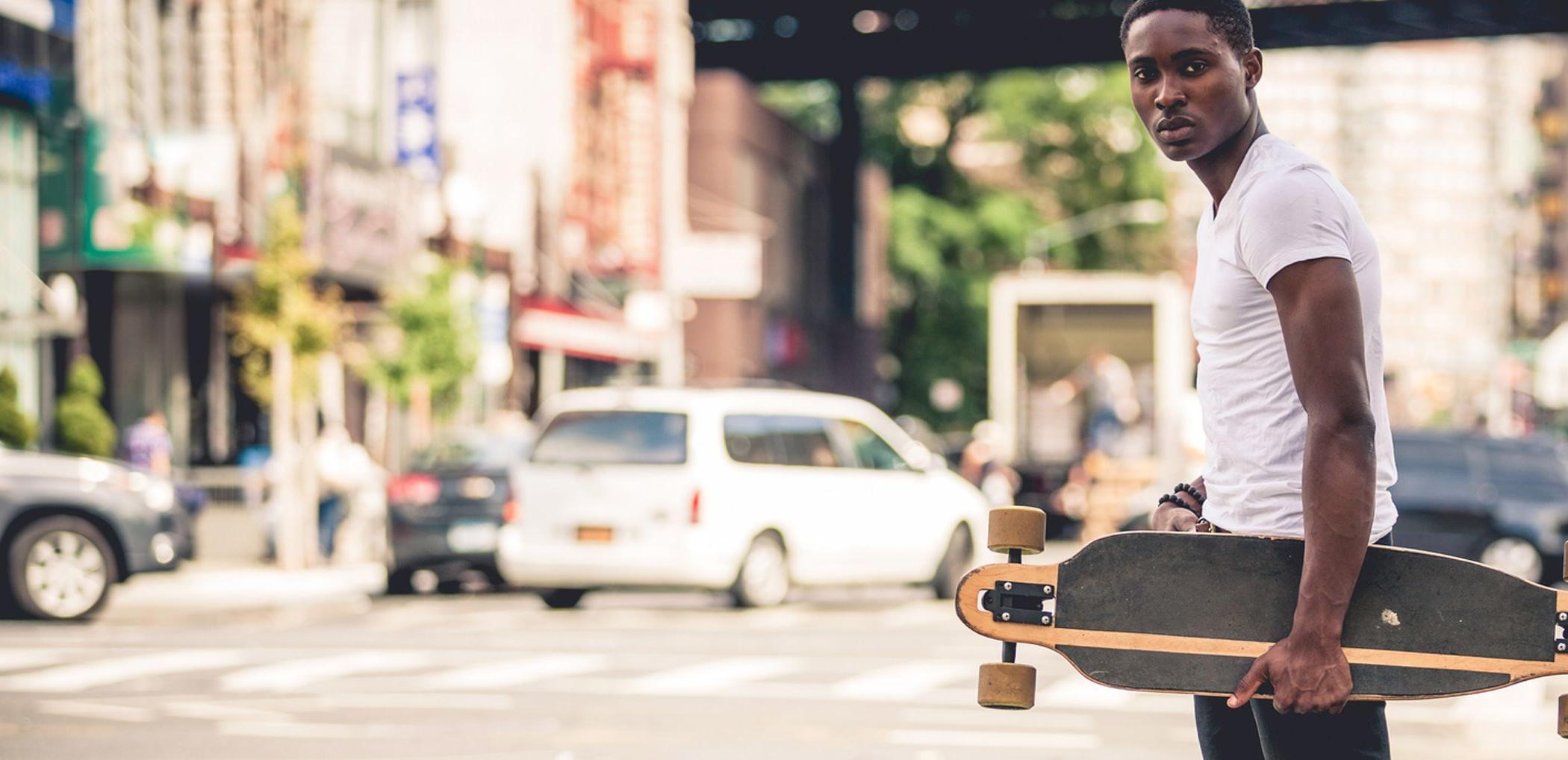 A teenager holds on to a skateboard as he crosses the street.